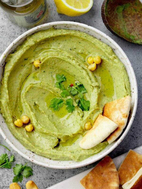 Creamy avocado hummus topped with olive oil, chickpeas, and fresh cilantro, served with pita bread.
