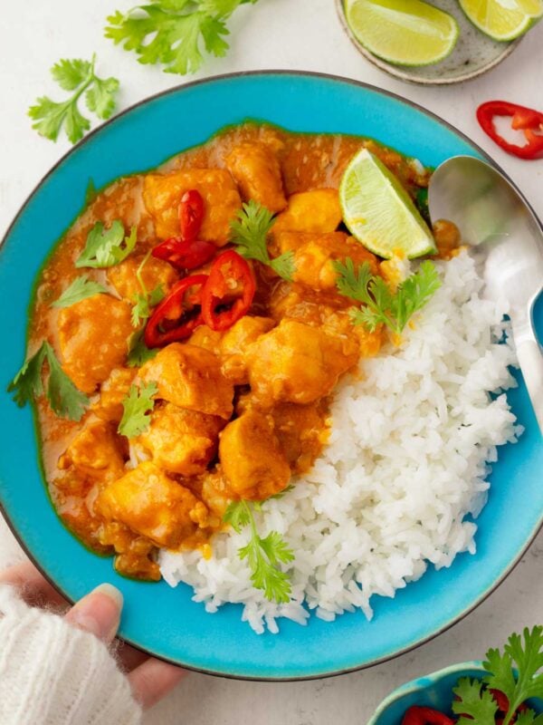 Thai coconut chicken curry served over jasmine rice with fresh cilantro, sliced red chili peppers, and lime wedges in a blue bowl.