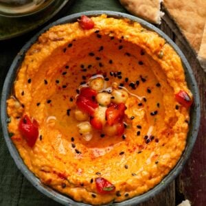 Roasted red pepper hummus topped with olive oil, chickpeas, and black sesame seeds, served with warm pita bread.