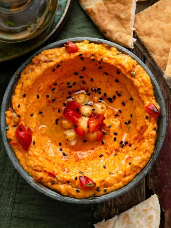 Roasted red pepper hummus topped with olive oil, chickpeas, and black sesame seeds, served with warm pita bread.
