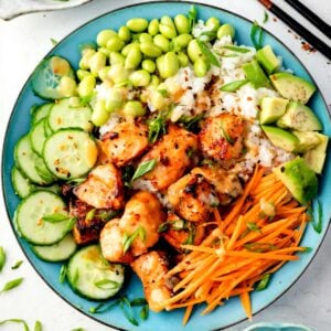 Air fryer miso salmon bowl with sushi rice, edamame, avocado, cucumber, shredded carrots, and scallions topped with creamy miso sauce.