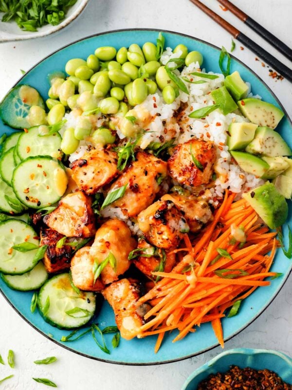 Air fryer miso salmon bowl with sushi rice, edamame, avocado, cucumber, shredded carrots, and scallions topped with creamy miso sauce.