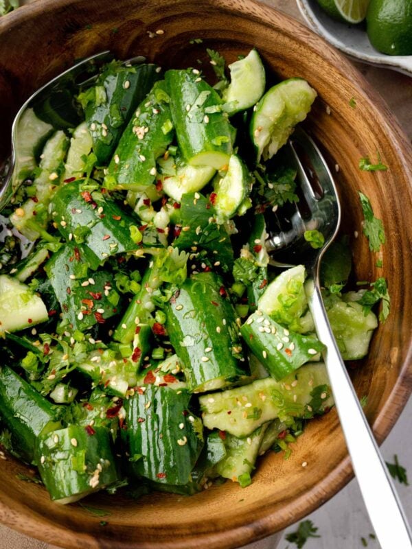 Smashed cucumber salad with sesame seeds, green onions, cilantro, and chili flakes in a wooden bowl with Asian-style dressing.