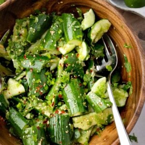 Smashed cucumber salad with sesame seeds, green onions, cilantro, and chili flakes in a wooden bowl with Asian-style dressing.