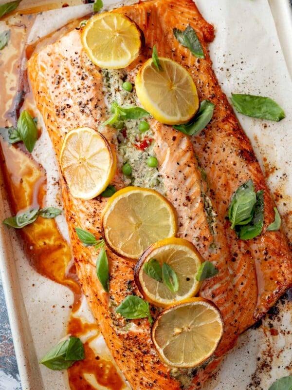 Mediterranean Stuffed Salmon baked with a creamy feta, spinach, pea, and sun-dried tomato filling, topped with roasted lemon slices and fresh basil leaves.