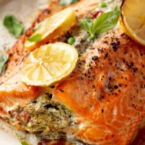 Close-up of Mediterranean Stuffed Salmon filled with creamy feta, spinach, peas, and sun-dried tomatoes, baked until flaky and topped with roasted lemon slices and fresh basil.