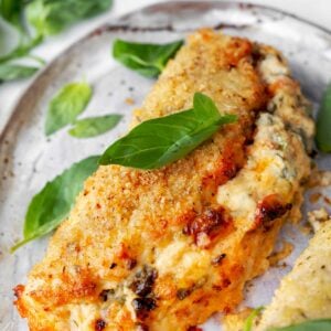 Crispy baked Boursin stuffed chicken breast with a creamy spinach and herb cheese filling, served hot and garnished with fresh basil leaves.