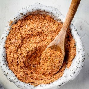 Close-up of homemade Old El Paso taco seasoning mix in a ceramic bowl with a wooden spoon, showing the fine texture of the spice blend.