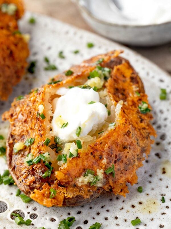 Parmesan crusted baked potato topped with sour cream, garlic-chive butter, and fresh chives, featuring a crispy golden Parmesan cheese crust and fluffy potato interior.