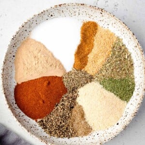 Ingredients for homemade potato seasoning arranged in a bowl, including paprika, garlic powder, onion powder, dried herbs, salt, and black pepper.