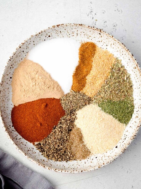 Ingredients for homemade potato seasoning arranged in a bowl, including paprika, garlic powder, onion powder, dried herbs, salt, and black pepper.