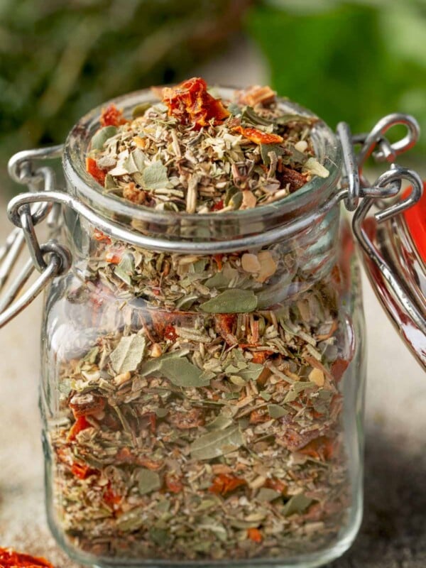 Homemade Tuscan seasoning in a glass spice jar, featuring dried herbs, garlic, and chopped sun-dried tomatoes. An easy Italian-inspired seasoning blend for chicken, pasta, vegetables, and soups.