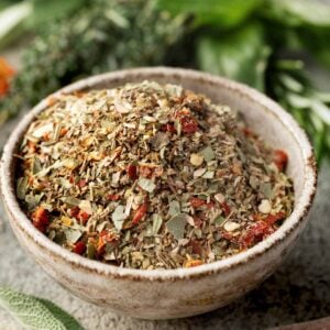 Homemade Tuscan seasoning blend in a rustic bowl, made with dried Italian herbs, garlic, onion, rosemary, sage, and chopped sun-dried tomatoes. Perfect for chicken, pasta, vegetables, and soups.