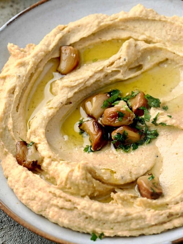 Creamy roasted garlic hummus topped with caramelized roasted garlic cloves, fresh parsley, and extra virgin olive oil, served in a shallow bowl.