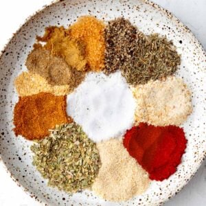 Homemade shrimp seasoning ingredients arranged in a white bowl, including paprika, garlic powder, onion powder, oregano, thyme, black pepper, cayenne, sea salt, celery salt, and spices before mixing.