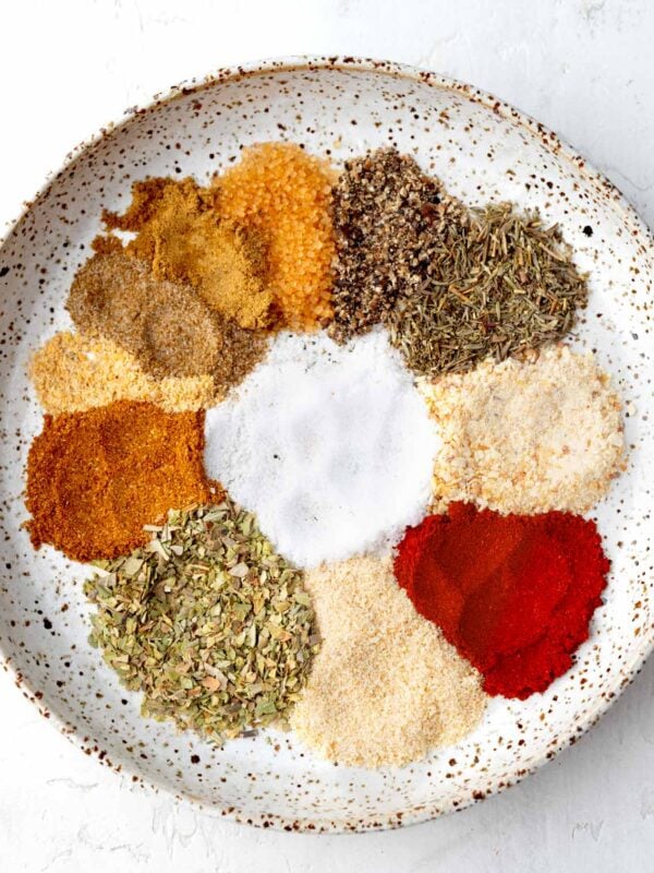 Homemade shrimp seasoning ingredients arranged in a white bowl, including paprika, garlic powder, onion powder, oregano, thyme, black pepper, cayenne, sea salt, celery salt, and spices before mixing.