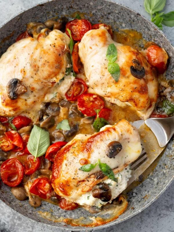 Stuffed Chicken Capri with creamy ricotta filling, melted mozzarella, mushrooms, cherry tomatoes, and fresh basil in a skillet.