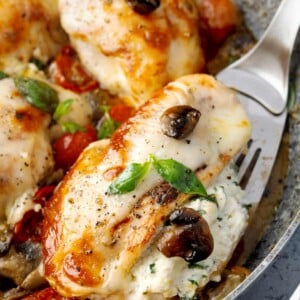 Close-up of Stuffed Chicken Capri with a creamy ricotta filling, melted mozzarella, mushrooms, cherry tomatoes, and fresh basil.