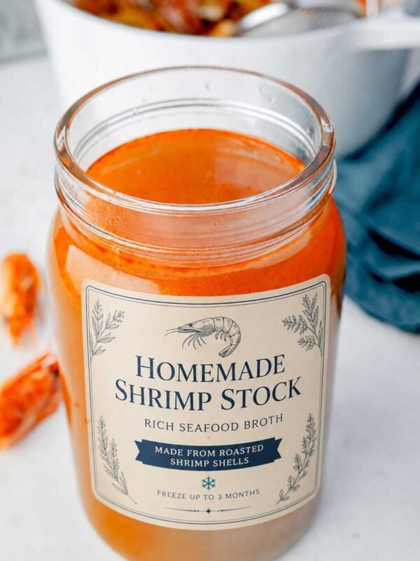 Jar of homemade shrimp shell broth with a rich golden-orange color after straining, ready to use for seafood soups, ramen, risotto, and sauces.