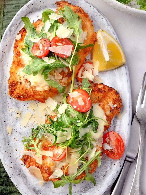 Crispy baked Chicken Milanese with melted mozzarella, arugula, cherry tomatoes, shaved Parmesan, and lemon wedges.