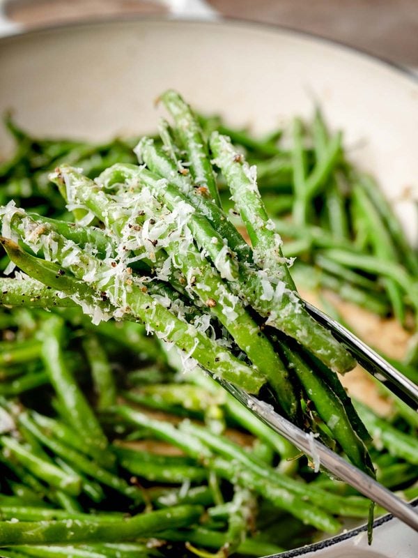 Cacio e pepe green beans coated with Pecorino Romano and cracked black pepper being served from a skillet.