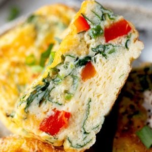 Cottage cheese egg muffin cut in half showing a fluffy interior with spinach, red bell pepper, and cheddar cheese.