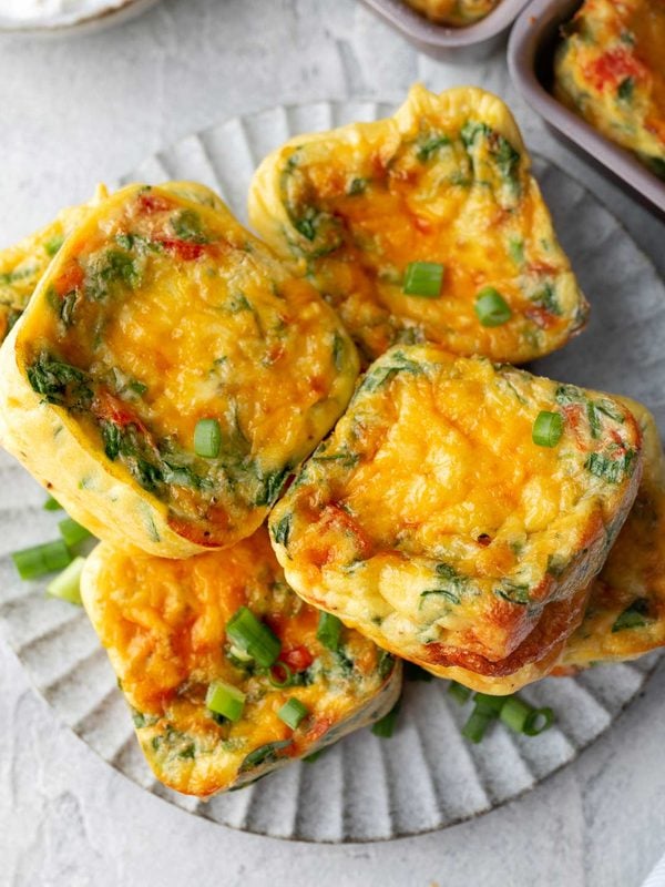 Cottage cheese egg muffins with spinach, red peppers, cheddar cheese, and green onions on a plate.