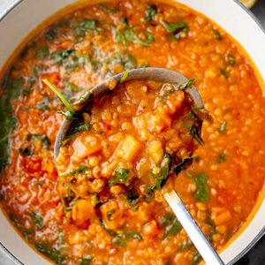 Italian red lentil soup with vegetables and spinach in a Dutch oven, served in a ladle.