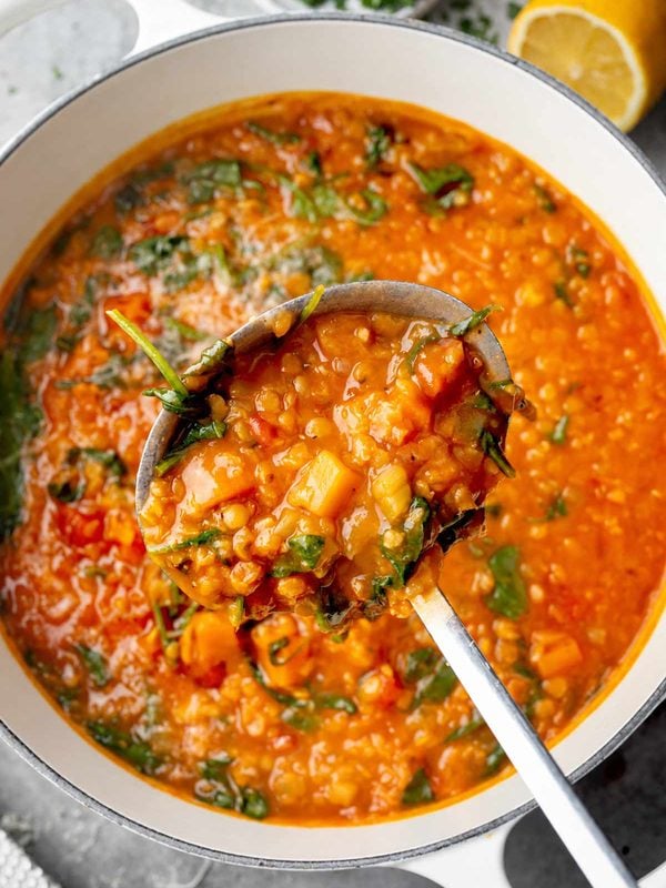 Italian red lentil soup with vegetables and spinach in a Dutch oven, served in a ladle.
