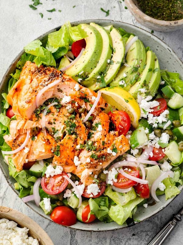 Salmon and avocado salad with romaine lettuce, cherry tomatoes, cucumber, feta, capers, red onion, and lemon.