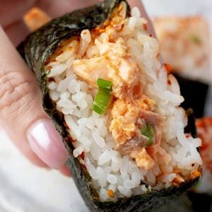 Salmon onigiri cut open to show creamy spicy salmon filling, Japanese rice, green onions, and nori.